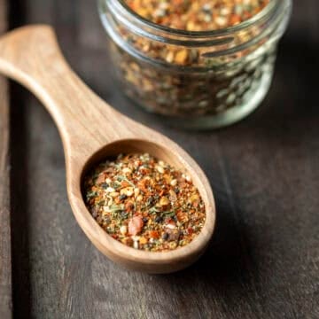 A wood spoon filled with homemade togarashi seasoning with a small jar full of the spice blend behind it.