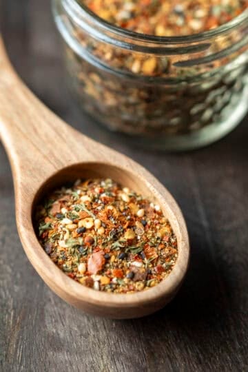 A wood spoon filled with homemade togarashi seasoning with a small jar full of the spice blend behind it.