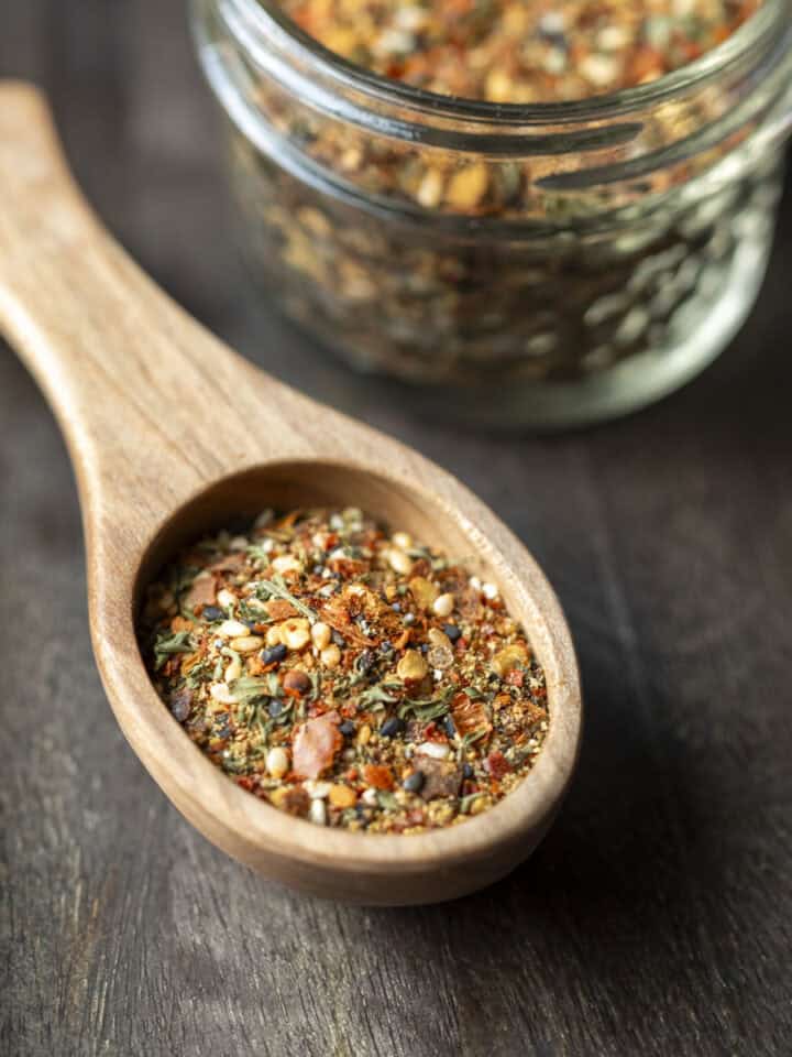 A wood spoon filled with homemade togarashi seasoning with a small jar full of the spice blend behind it.