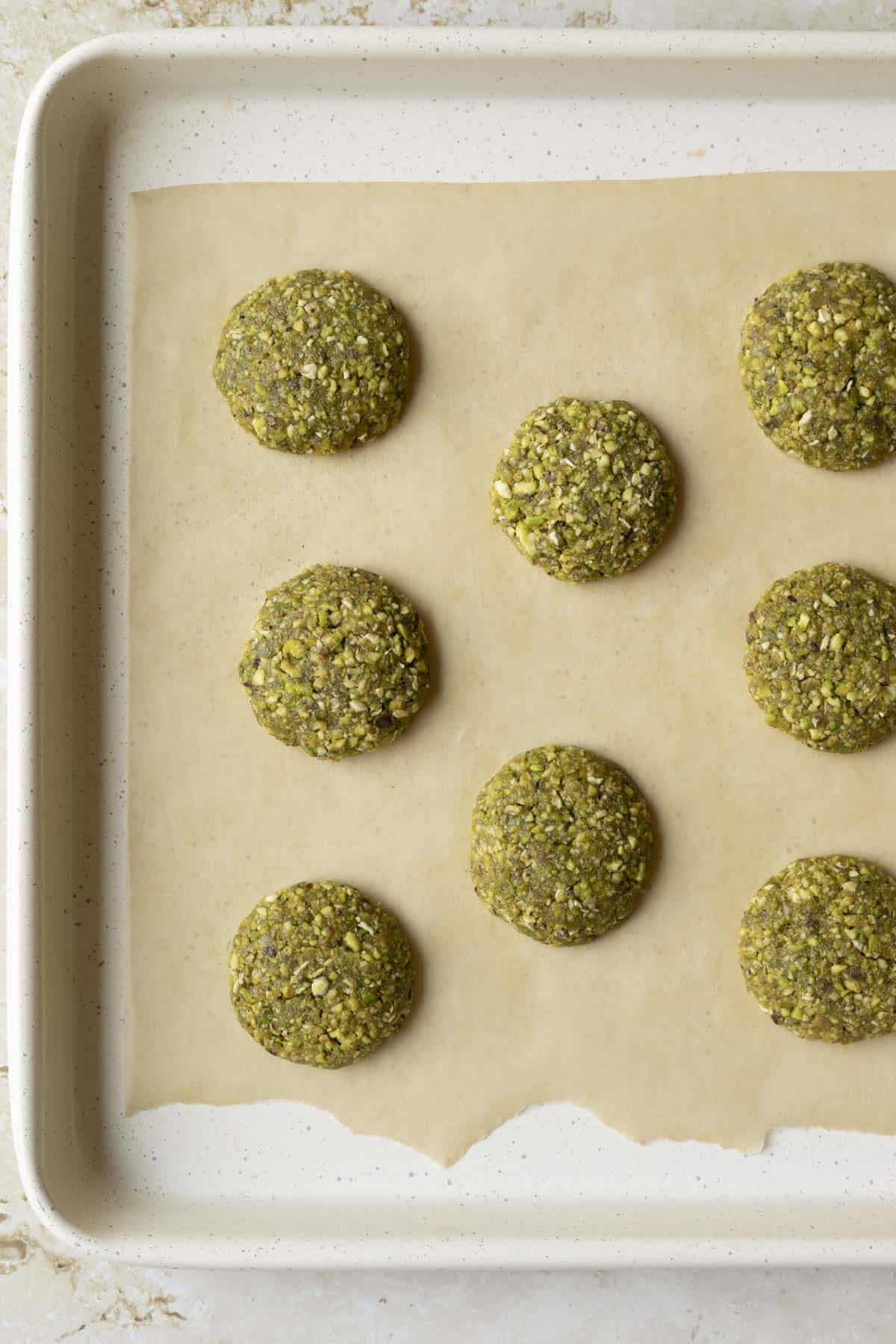 Shaped pistachio cookie dough on a parchment-lined baking sheet.