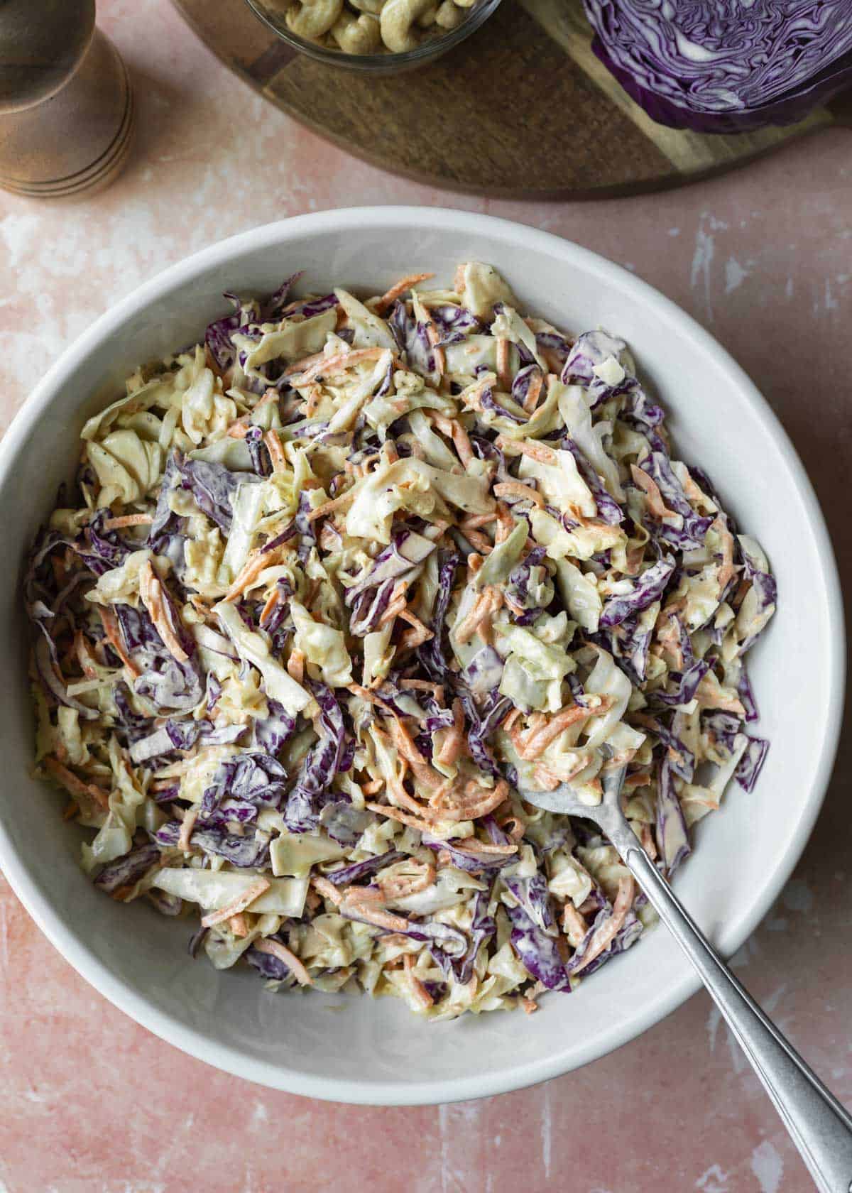 Overhead of colorful and creamy vegan slaw in a white serving bowl.