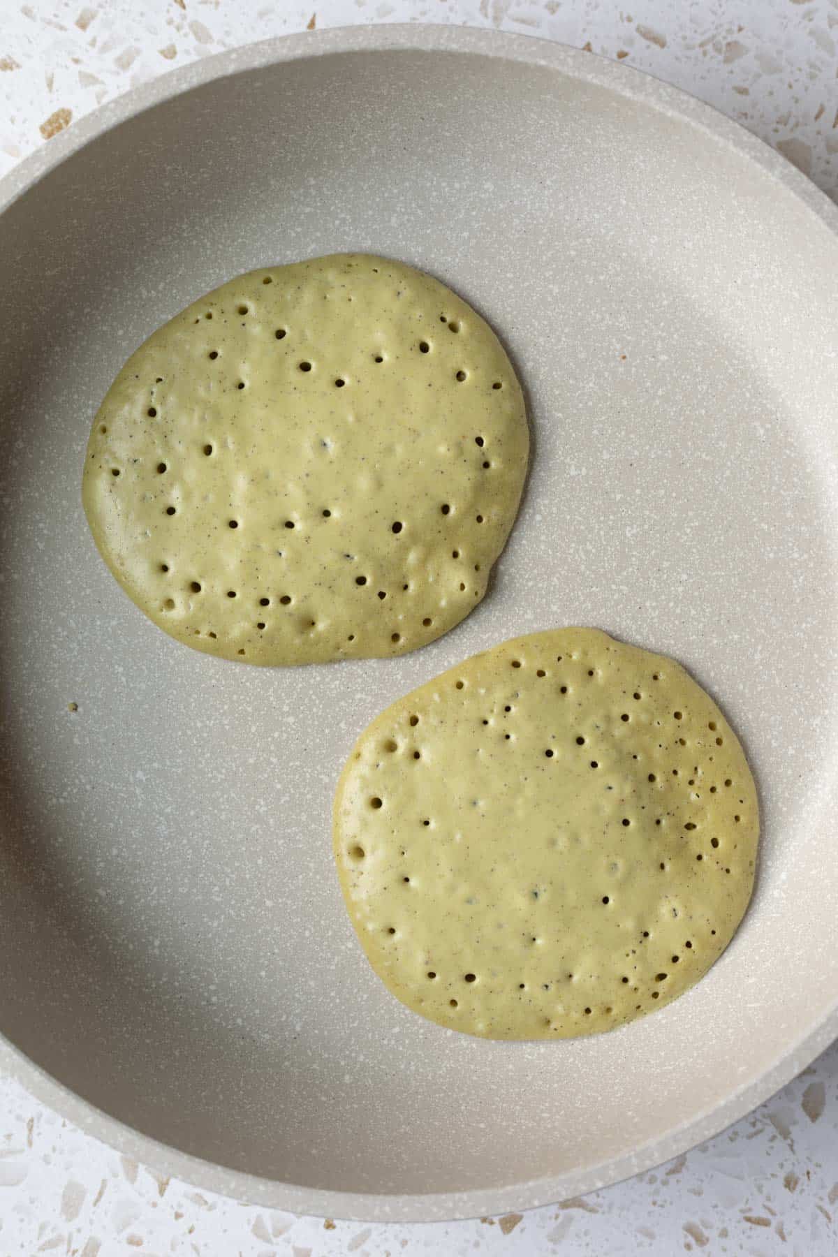Pancakes in a non-stick pan with bubbles across top demonstrating when ready to be flipped.