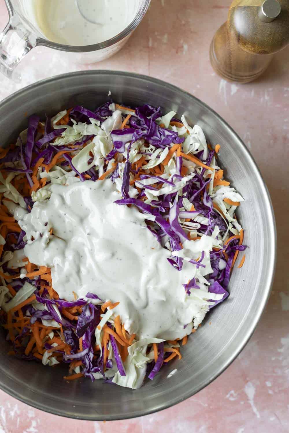 Combining shredded cabbage and carrot with vegan coleslaw dressing in a large bowl.