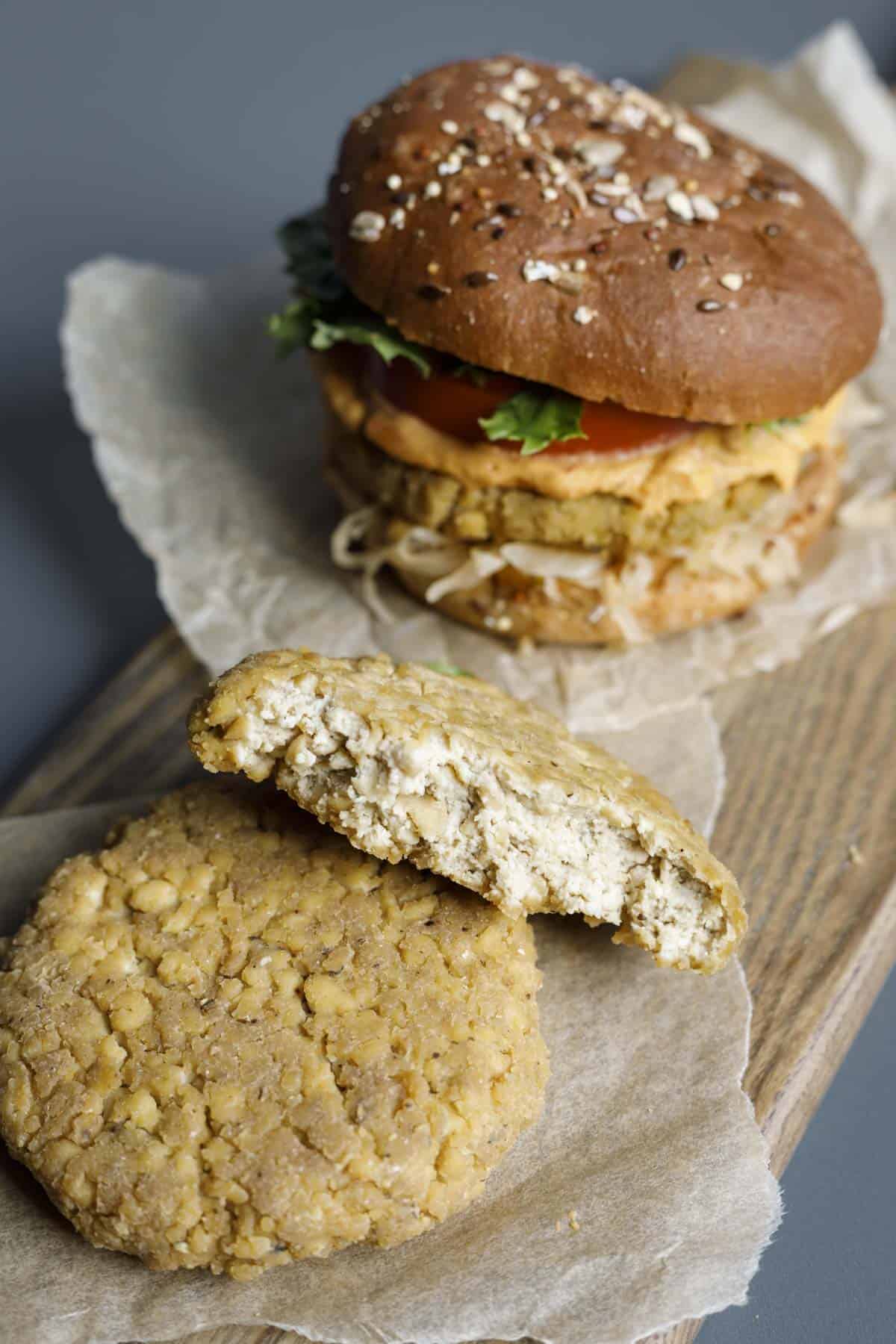 Tofu chicken patty cut in half to show the texture and a dressed tofu burger on a wooden board.