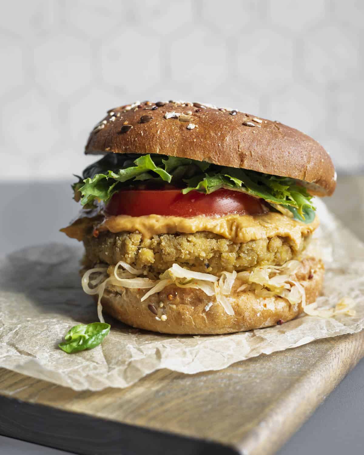 A tofu burger on whole grain bun resting on a wooden cutting board.
