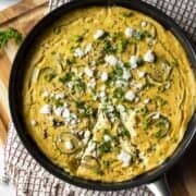 Baked vegan frittata in a pan topped with feta, green onion, and parsley.