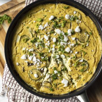 Baked vegan frittata in a pan topped with feta, green onion, and parsley.