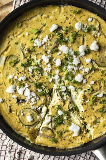 Baked vegan frittata in a pan topped with feta, green onion, and parsley.