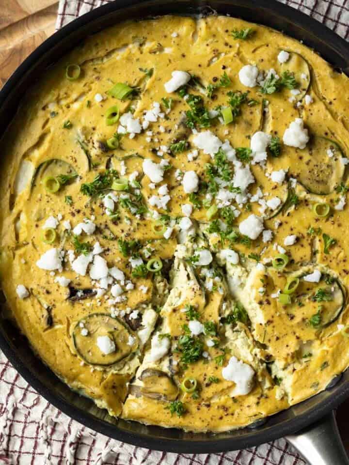 Baked vegan frittata in a pan topped with feta, green onion, and parsley.