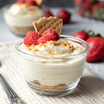 A small glass cup filled with cheesecake pudding with graham crumbs on bottom and fresh berries on top.
