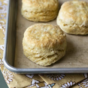Three tall and flaky vegan biscuits on a baking sheet.