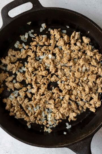 Sauteing onion and browning crumbled vegan sausage in a skillet.
