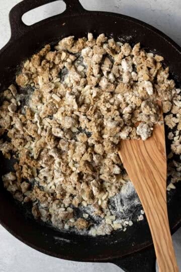 Adding flour to the skillet which thickens the white gravy.