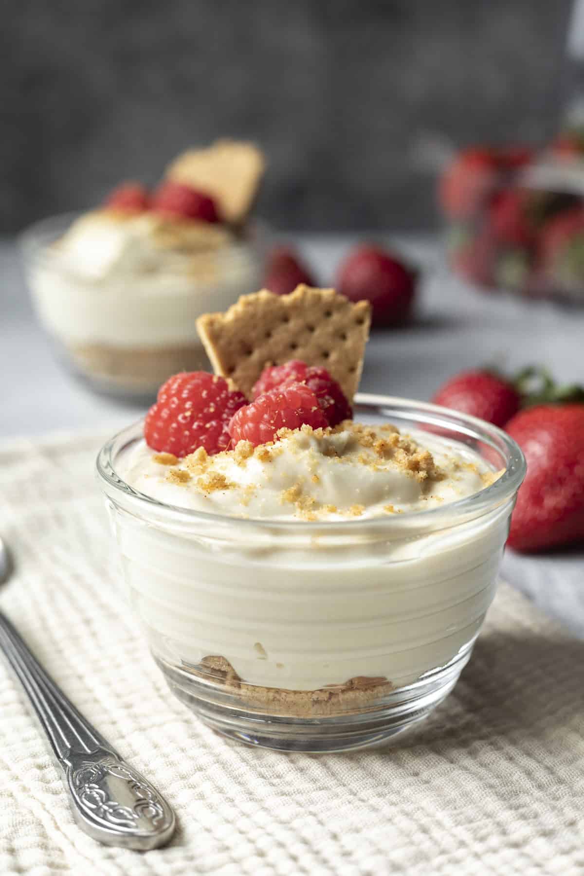 Vegan cheesecake pudding in a glass cup with another serving in the backgrouund.