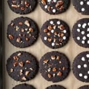 Black cocoa cookies topped with white chocolate chips and chopped pecans resting on parchment paper.