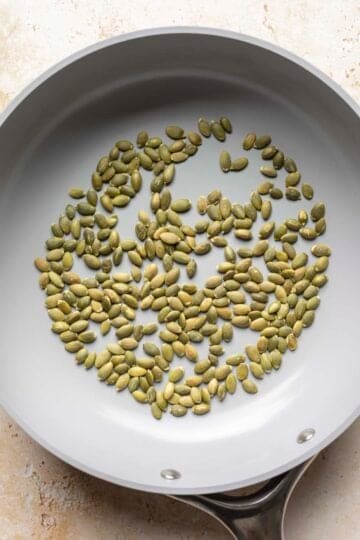 Toasting pumpkin seeds in a dry pan on the stovetop.
