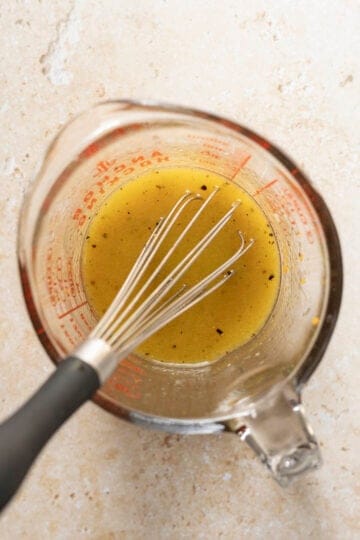 Whisking ingredients for orange vinaigrette in a glass measuring cup.