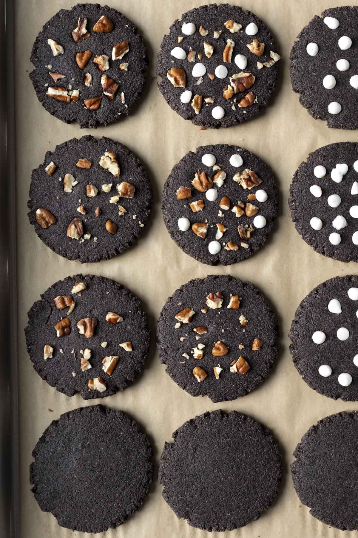 A dozen black cookies on a parchment paper lined baking sheet.
