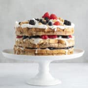 French toast cake with yogurt and berries on a white cake stand.