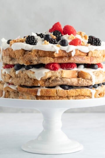 French toast cake with yogurt and berries on a white cake stand.