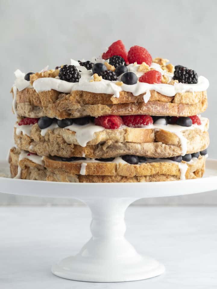 French toast cake with yogurt and berries on a white cake stand.