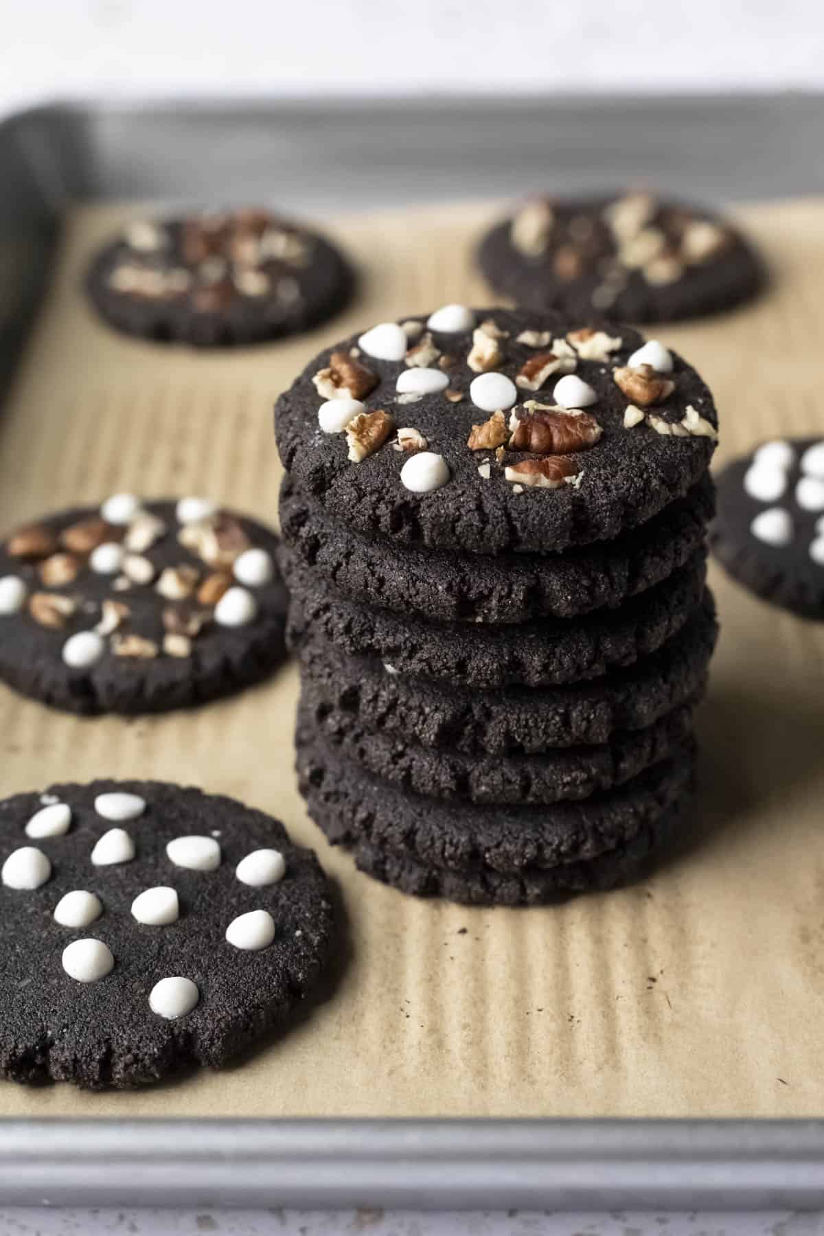 A stack of 7 black cookies with nuts and white chocolate chips on top.