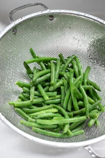 Green beans draining in a colander after being rinsed with cold water.