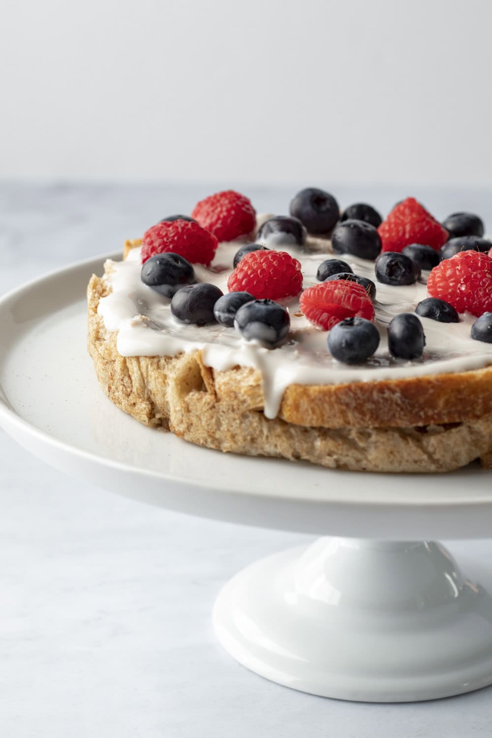 One layer on a cake stand topped with yogurt and mixed berries.