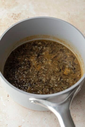 Wild rice cooked in broth inside a pot, ready to be drained.