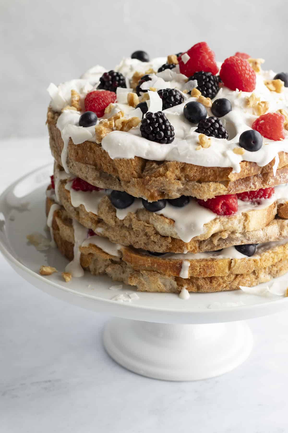 Three layer decorated french toast cake with yogurt, berries, walnuts, and whipped cream.