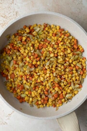 Frozen corn kernels added to the sauteed vegetables in the pan.