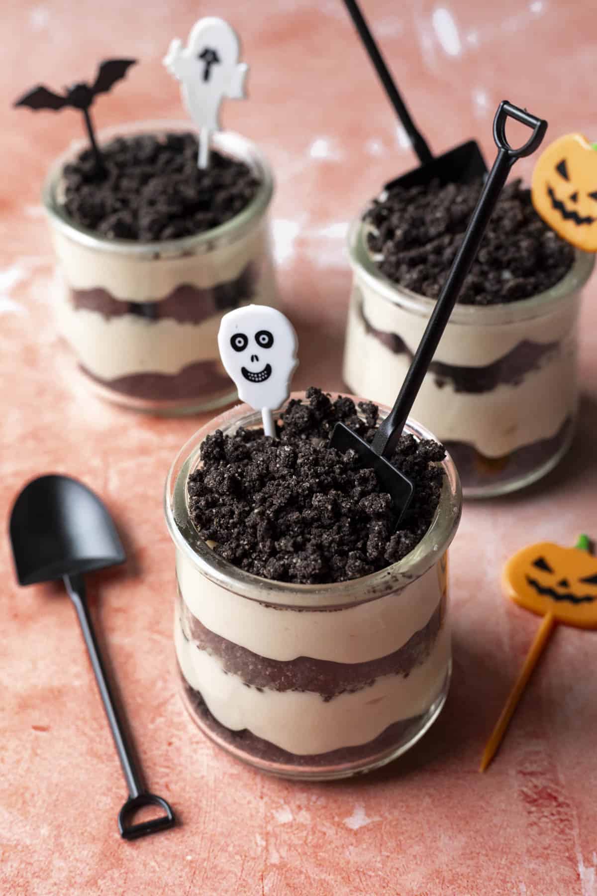 Individual dirt cups with Halloween decorations on an orange background.