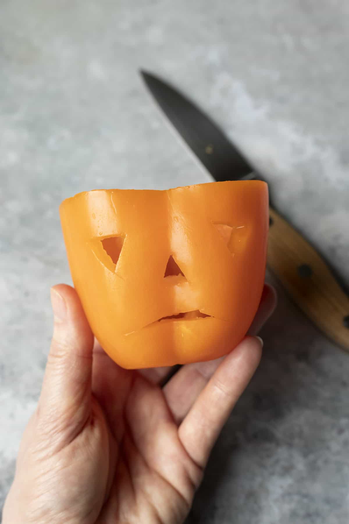 Carving eyes, nose, and mouth in an orange pepper with a paring knife.