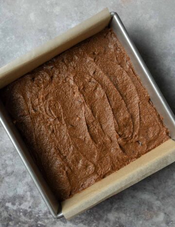 Thick pumpkin brownie batter spread in a parchment-lined baking pan.