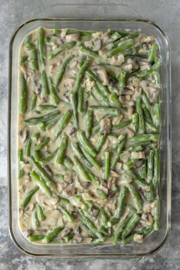 Green beans and creamy mushroom sauce poured into a 13 by 9 inch casserole dish.