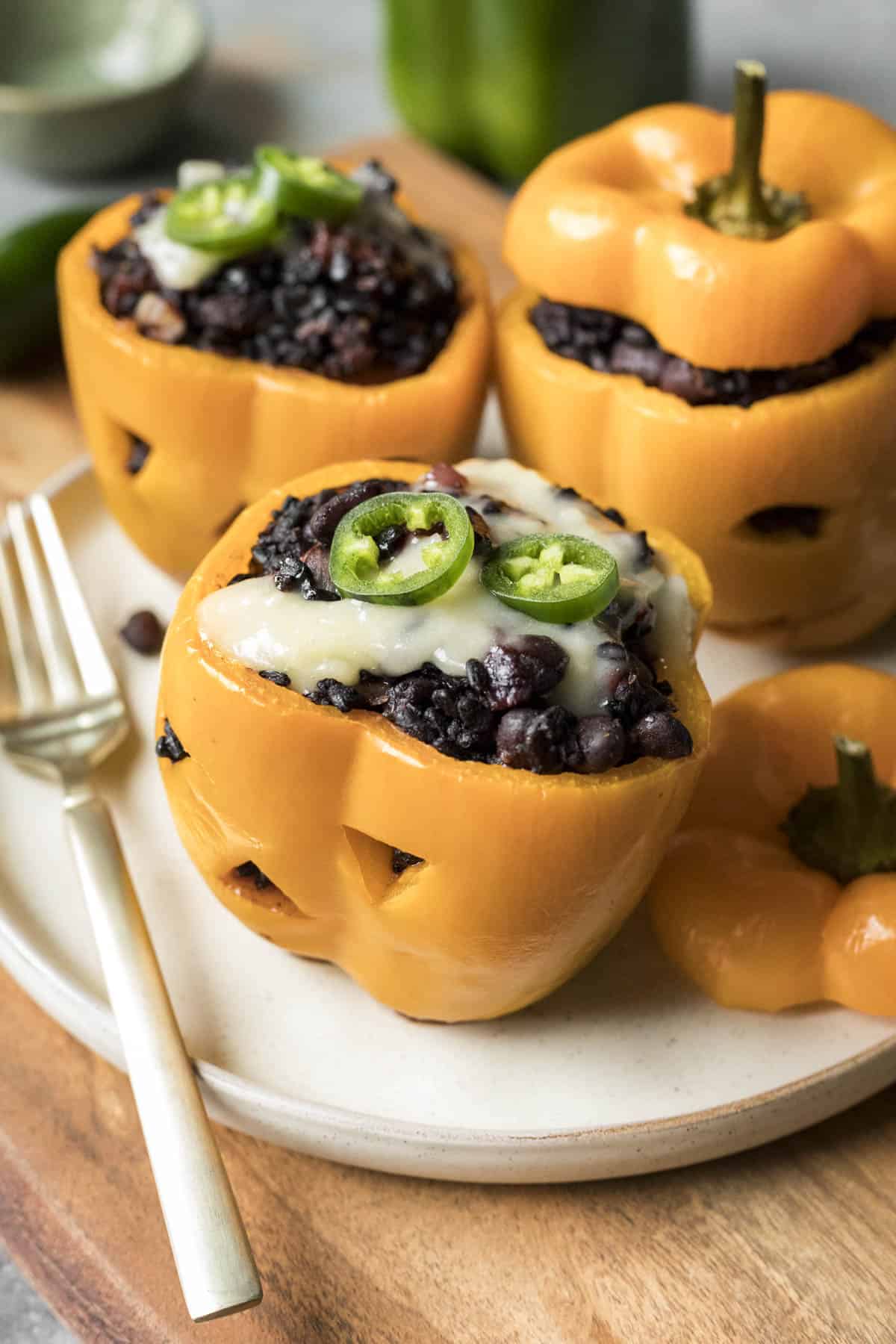 Three halloween stuffed peppers on a plate topped with cheese and jalapeno.