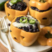 Stuffed orange bell peppers carved like pumpkins and filled with black rice and beans.
