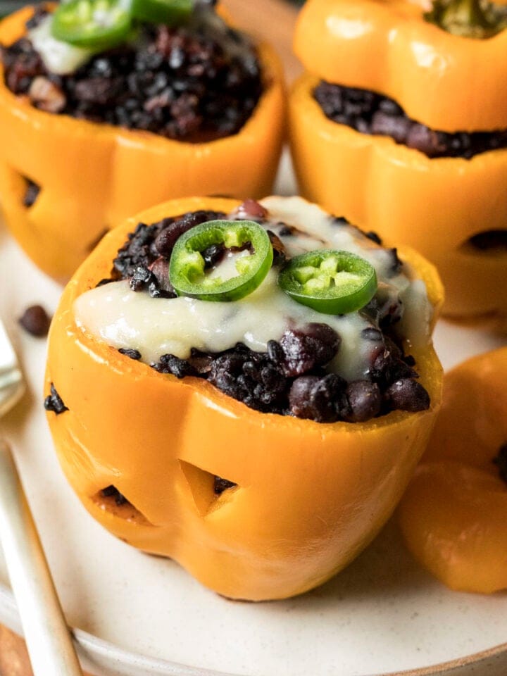 Stuffed orange bell peppers carved like pumpkins and filled with black rice and beans.