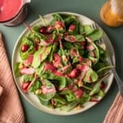 A mixed greens salad on a plate dressed with colorful pink cranberry dressing.