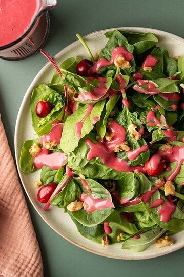 A mixed greens salad on a plate dressed with colorful pink cranberry dressing.