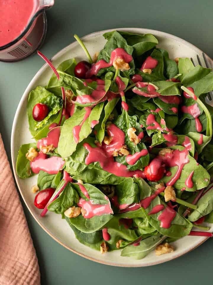 A mixed greens salad on a plate dressed with colorful pink cranberry dressing.