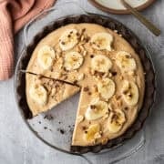 Overhead view of peanut butter cream pie topped with sliced banana, peanuts and chocolate.