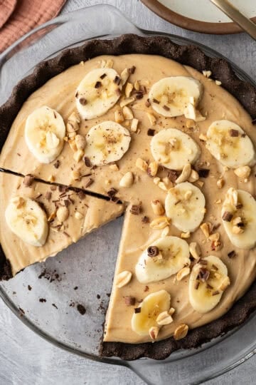 Overhead view of peanut butter cream pie topped with sliced banana, peanuts and chocolate.