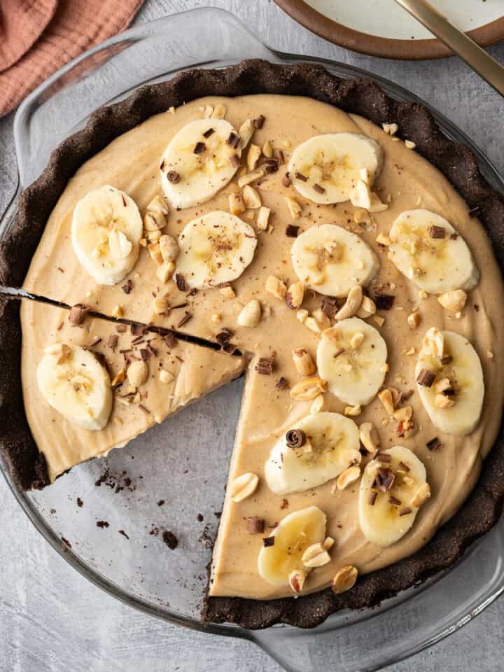 Overhead view of peanut butter cream pie topped with sliced banana, peanuts and chocolate.