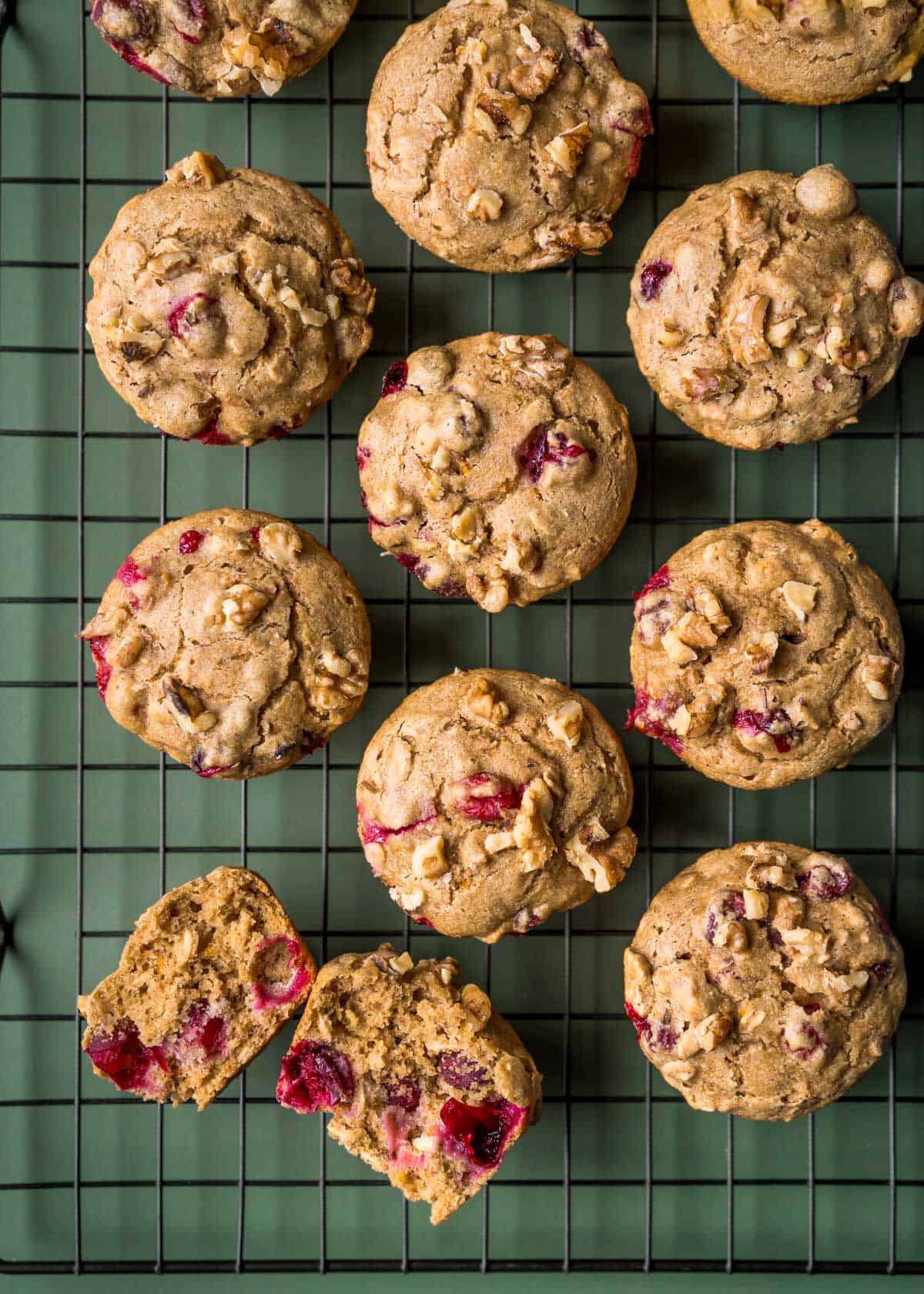 Muffins on a cooling rack with one cut in half to show the fluffy texture and burst cranberries.