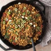 Moroccan quinoa topped with olives and parsley being served from a cast iron pan.