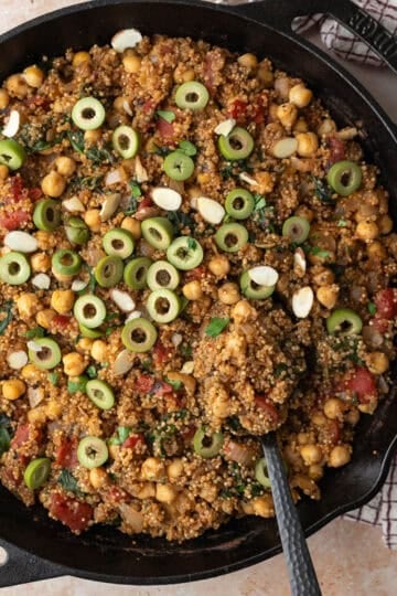 Moroccan quinoa topped with olives and parsley being served from a cast iron pan.