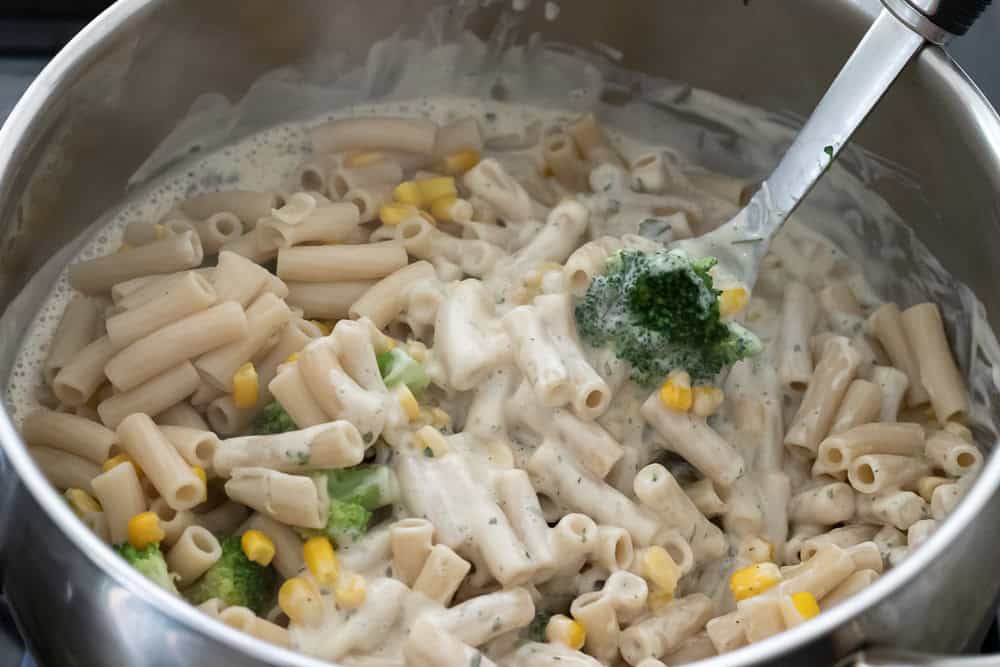 Tossing the heated ranch sauce with pasta and vegetables.