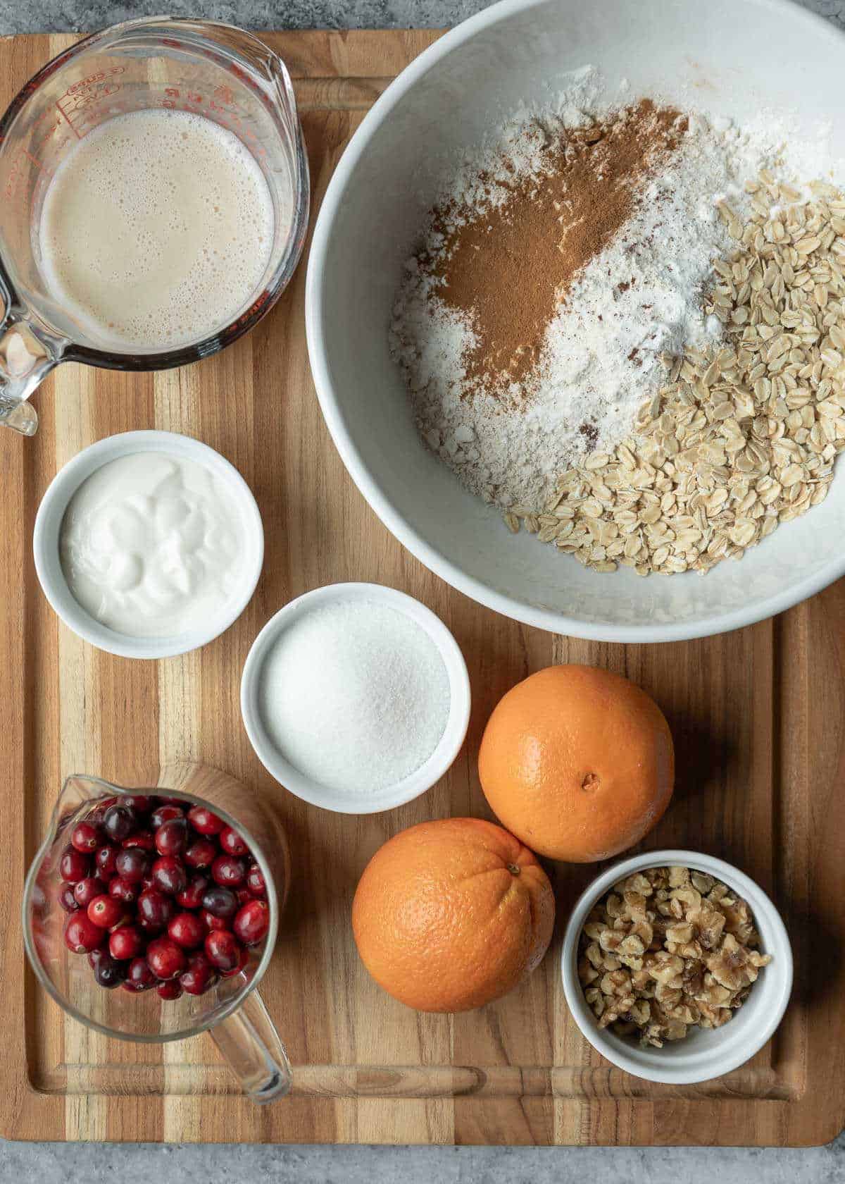 Ingredients for orange cranberry muffins on a wood cutting board.
