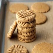 A stack of six peanut butter powder cookies on a parchment-lined baking sheet.